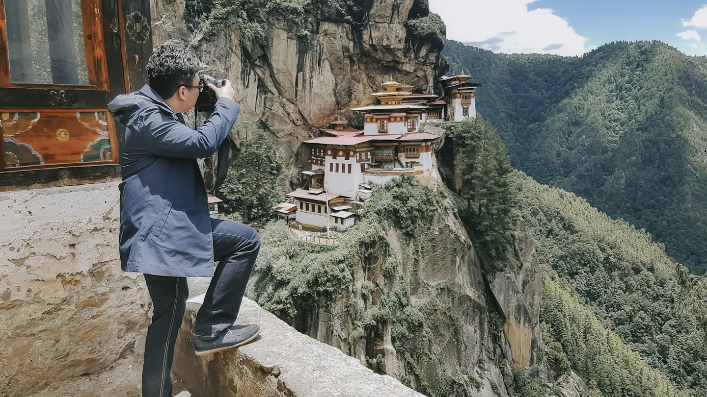 An Asian tourist photographing the Tiger's Nest Monastery in Bhutan