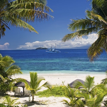 Sail boat seen through palm trees, Mamanuca Group islands, Fiji