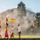 A mother and a teenaged girl are dressed in brightly colored sarongs, blouses, and sashes and are balancing tall fruit baskets on their heads. Two sons are dressed in sarongs and white shirts. The family is walking in front of an old stone temple building which has a smoky atmosphere.
938016384
religious