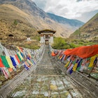 Tachog Lhakhang Iron Chain Bridge with colourful prayer flags on each side of bridge. River crossing. Himalaya mountains in the background.Between Paro and Thimphu Bhutan