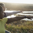 Two women practising a yoga pose (warrior 2) outdoors on a sunny afternoon.