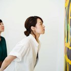 Two women standing in an art gallery, looking at an abstract modern painting. - stock photo