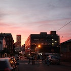 A shot of an intersection, with a bright pink-and-orange sky backing the surrounding buildings and traffic © Heather Mason / Lonely Planet