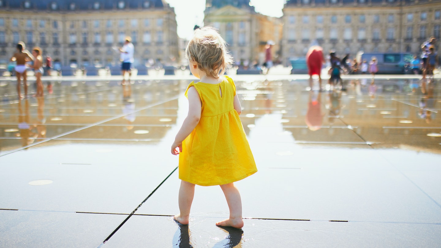 A toddler in a yellow sundress playing in the Miroir d'Eau in Bordeaux