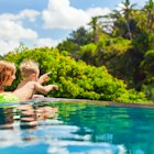 Family Bali beach holiday concept. Happy son with mother - active baby at poolside in infinity swimming pool. Summer healthy lifestyle and children water activity, games and lessons with parents.