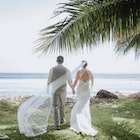 Wedding Couple Walking towards Ocean with Breeze Catching Veil